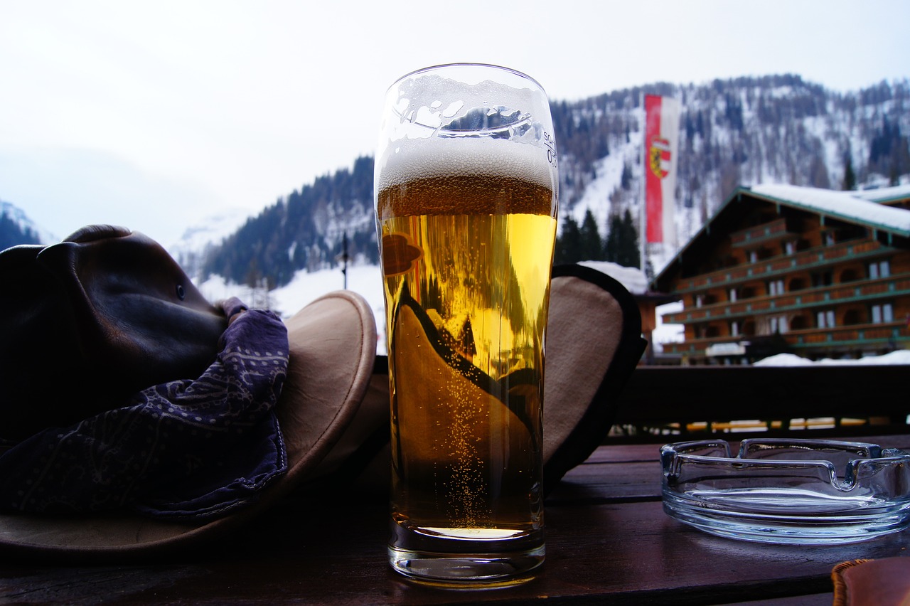 A glass of beer in the foreground with a snowy lodge in the background